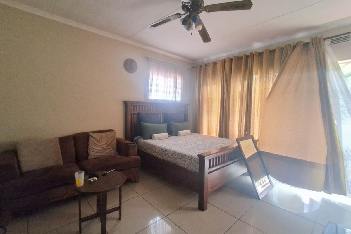 A bedroom featuring tiled flooring, a ceiling fan, and large windows with curtains, providing access to an outdoor area.
