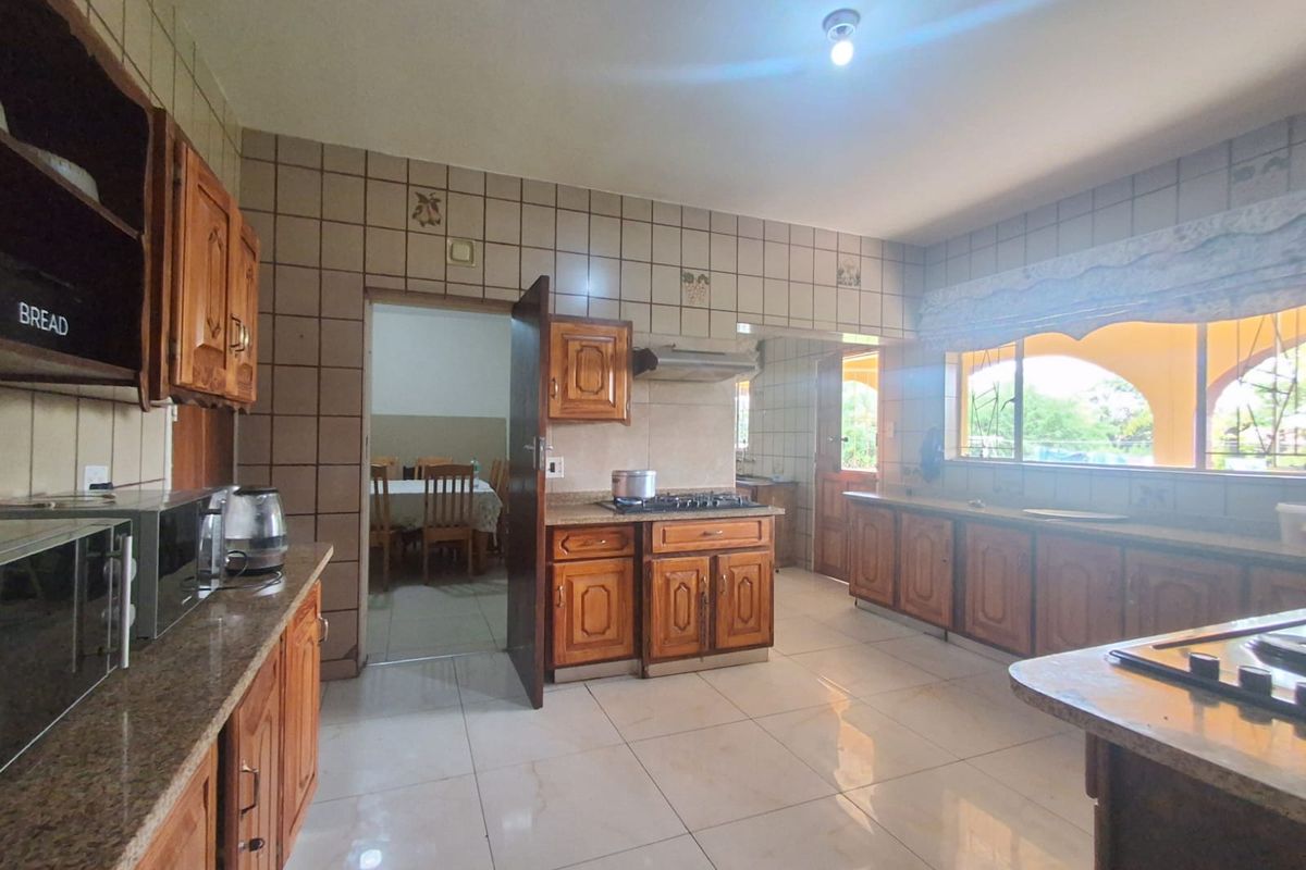 Spacious kitchen featuring wooden cabinetry, granite countertops, built-in gas hob, and extractor fan, with tiled flooring and direct access to adjacent dining area.
