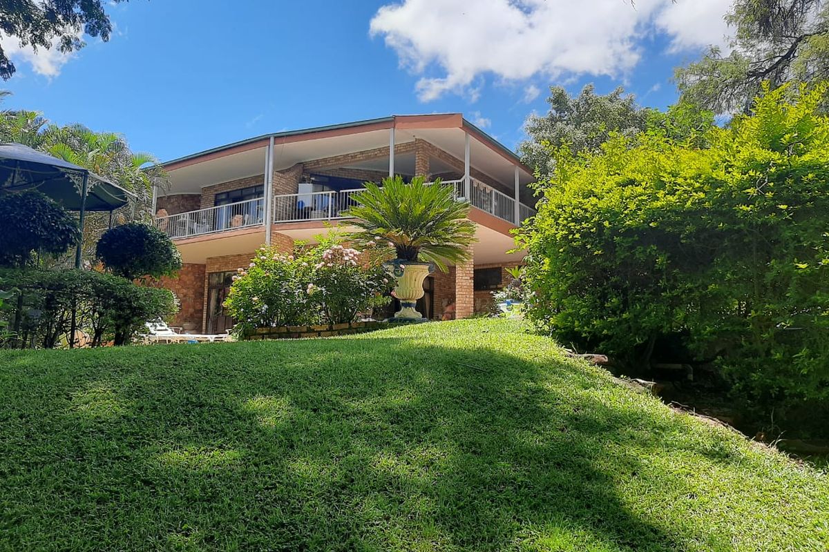 A view of the rear elevation of a two-story brick house featuring a spacious covered balcony and a well-maintained garden.