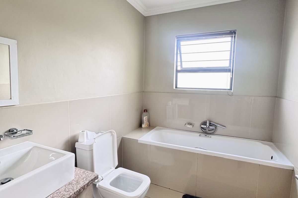 A well-maintained bathroom featuring a built-in bathtub, a modern vanity with a basin, and a toilet, finished with neutral wall and floor tiles.