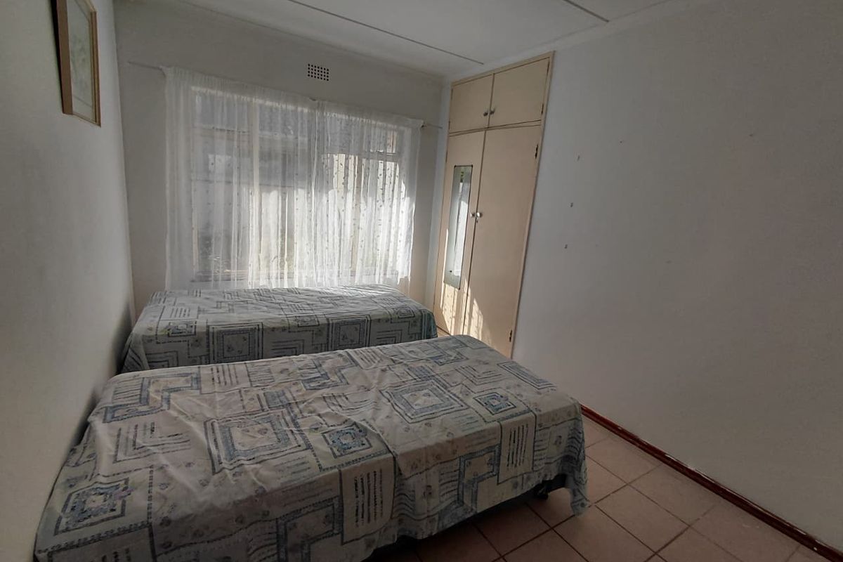 A functional bedroom featuring built-in cupboards, tiled flooring, and a window with natural light.
