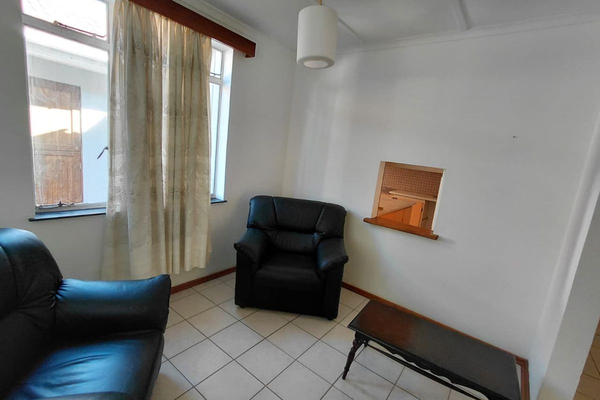 A compact living area featuring tiled flooring and a serving hatch connecting to the kitchen space.