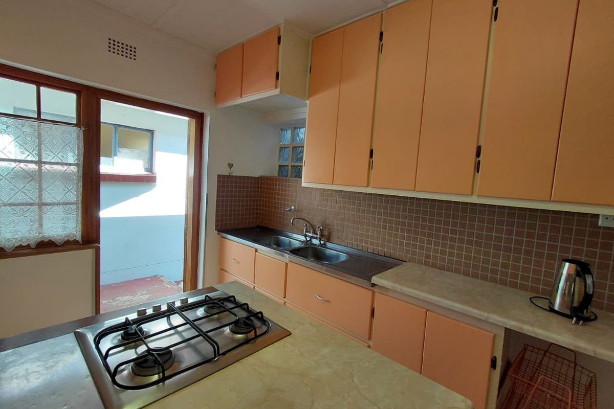 A dated kitchen featuring peach-toned cabinetry, a built-in gas hob, stainless steel double sink, and direct access to an outdoor area.