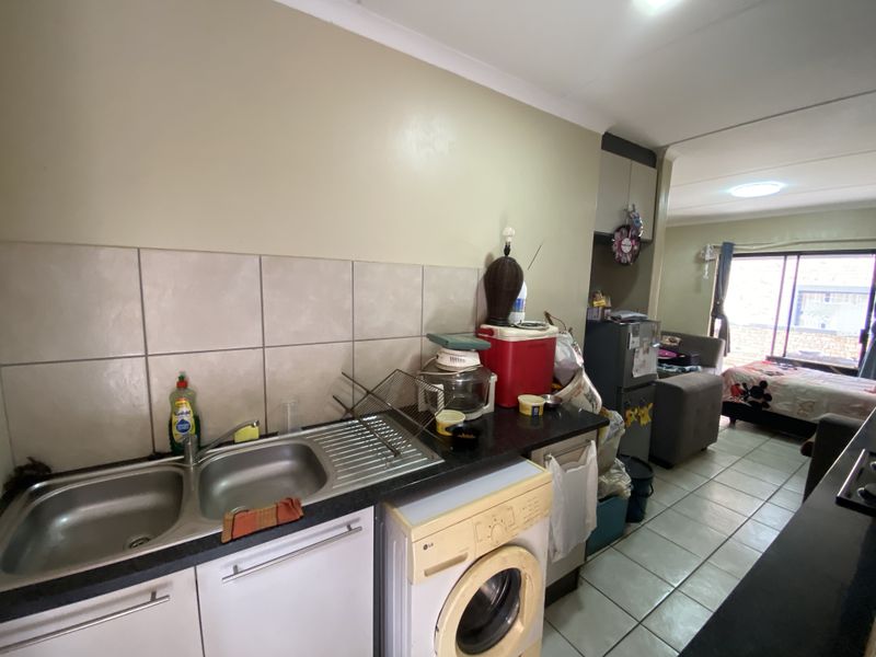 Compact kitchen area featuring a double stainless steel sink, tiled backsplash, and integrated laundry plumbing, flowing into an adjacent living space.
