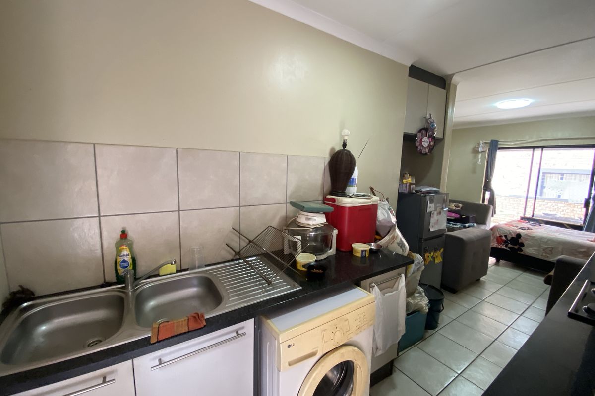 Compact kitchen area featuring a double stainless steel sink, tiled backsplash, and integrated laundry plumbing, flowing into an adjacent living space.