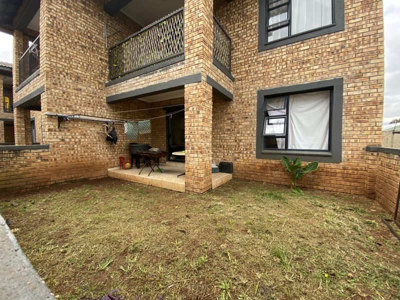 Rear view of a townhouse featuring a covered patio, brick facade, upper balcony with metal railing, and a private garden area.