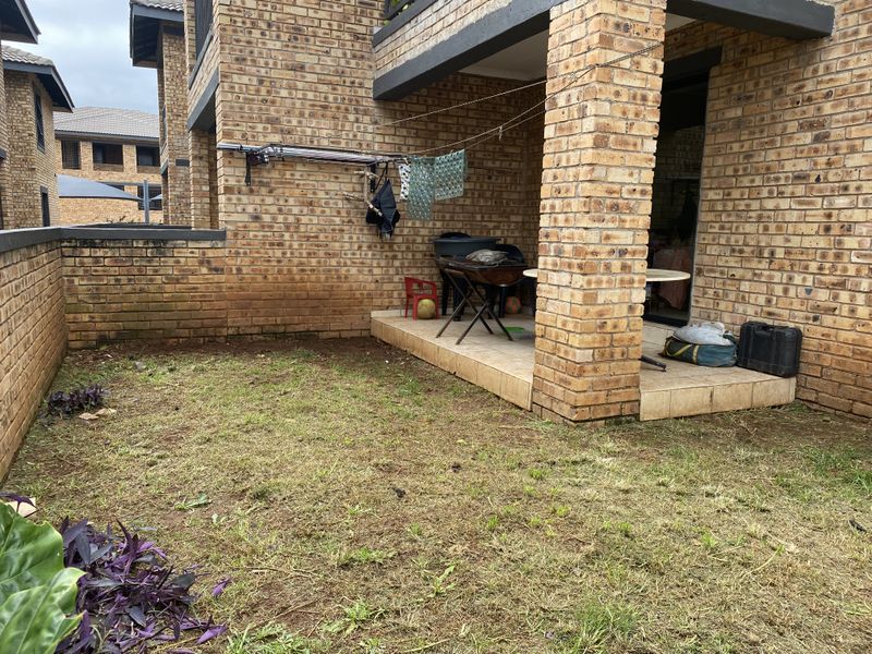 A private rear garden area featuring a tiled patio, face-brick exterior walls, and a small lawn space, providing a functional outdoor living area.