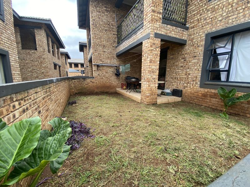 A private rear garden area featuring a covered patio, face-brick exterior walls, and a small lawn space within a townhouse complex.