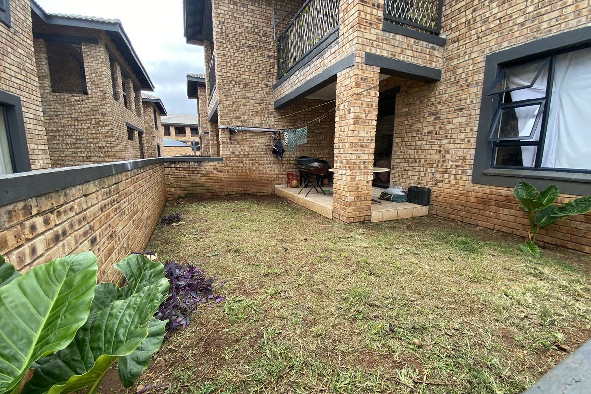 A private rear garden area featuring a covered patio, face-brick exterior walls, and a small lawn space within a townhouse complex.