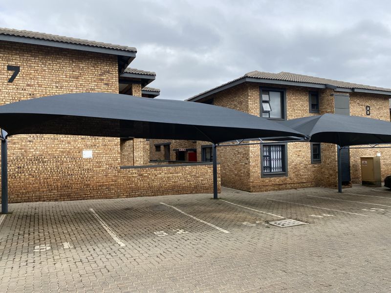 Exterior view of a townhouse complex featuring face-brick facades and covered shade-cloth parking bays.