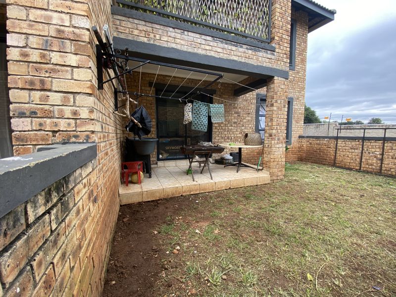 A covered patio area with tiled flooring, brick exterior walls, and a wall-mounted drying rack, overlooking a small private garden space.