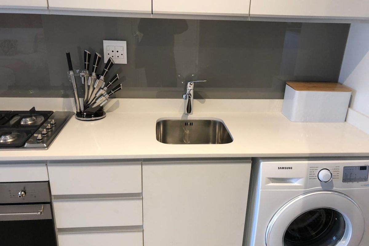 Modern kitchen featuring white cabinetry, stone countertops, a glass splashback, integrated gas hob, built-in oven, and a stainless steel sink.