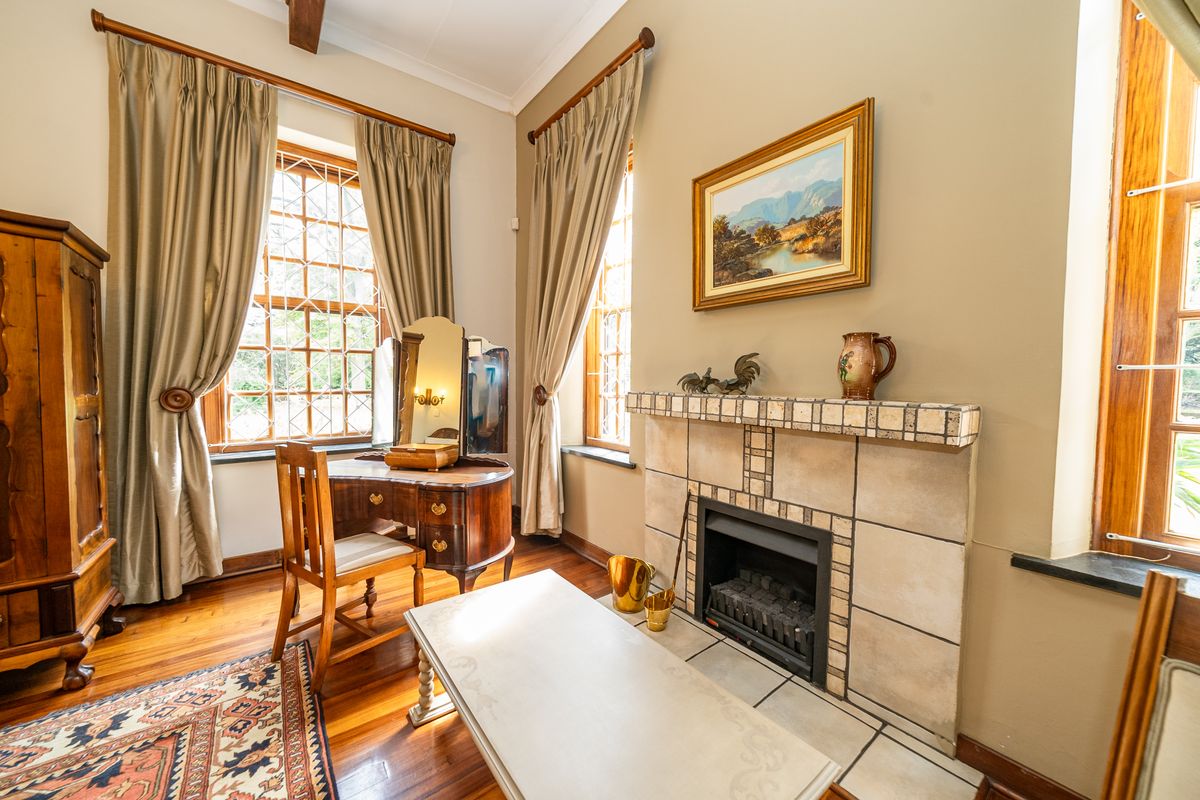 A cozy bedroom featuring polished wooden flooring, a tiled fireplace surround, and large windows with security bars, offering a warm and inviting atmosphere.