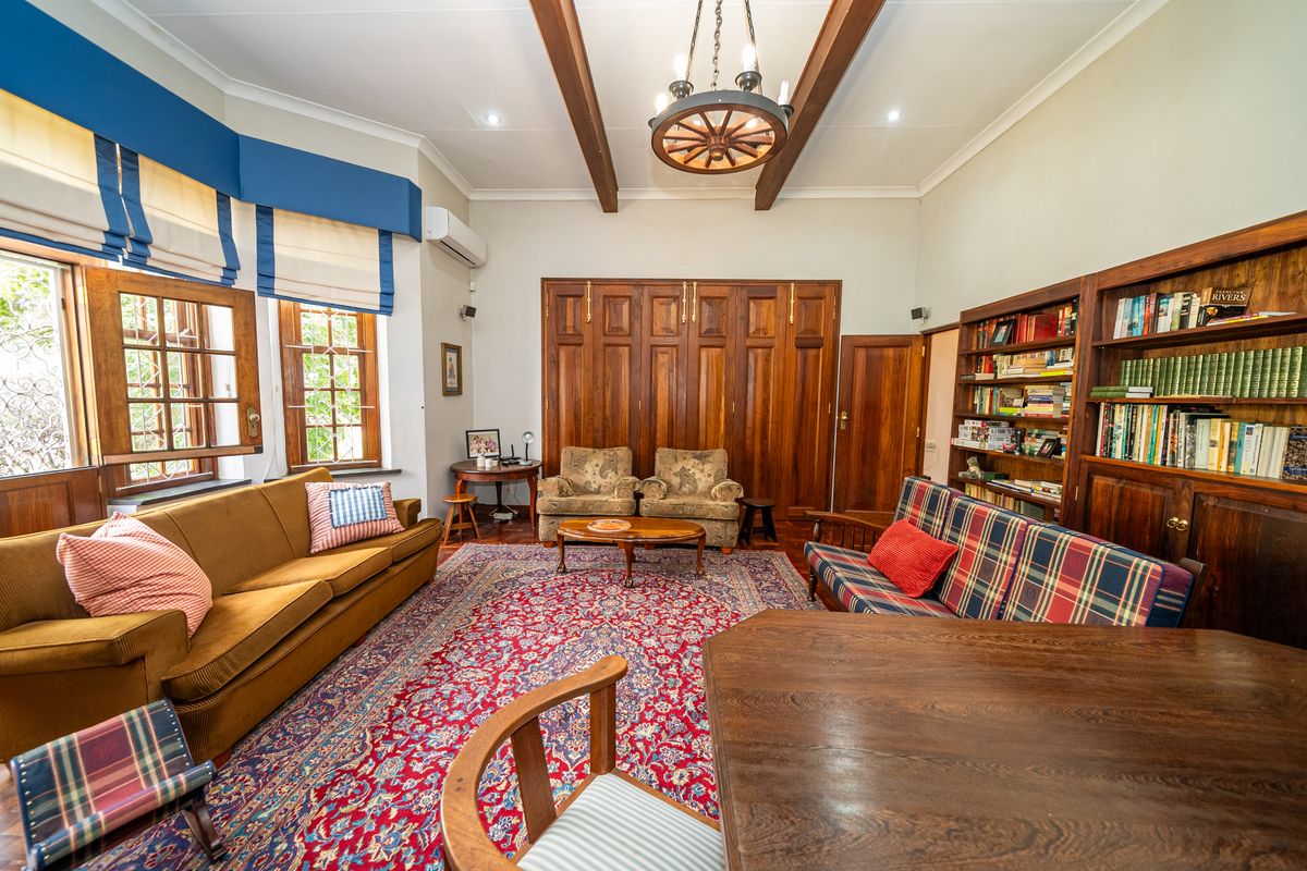 Spacious living room featuring exposed timber ceiling beams, built-in wooden cabinetry, and large windows with classic timber frames.