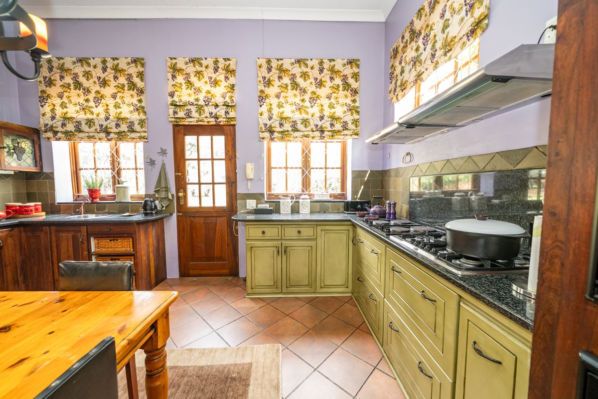 A traditional kitchen featuring olive green cabinetry, granite countertops, a gas hob with extractor fan, and terracotta floor tiles.