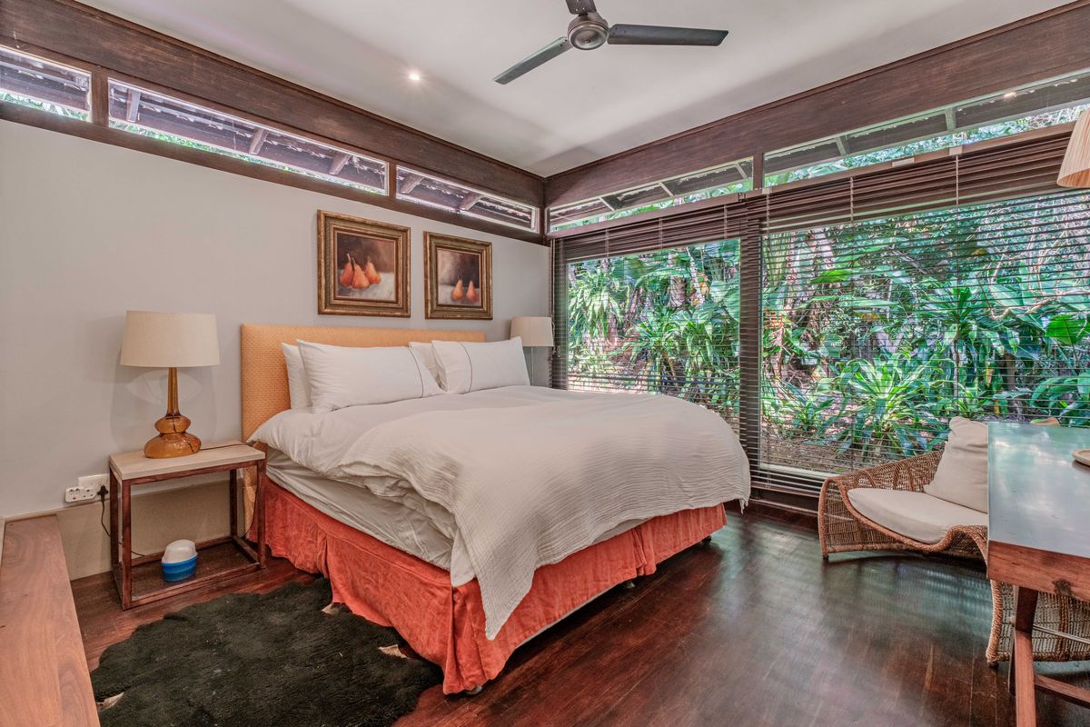 A well-lit bedroom featuring dark timber flooring, high-level clerestory windows, and large floor-to-ceiling windows overlooking a lush garden.