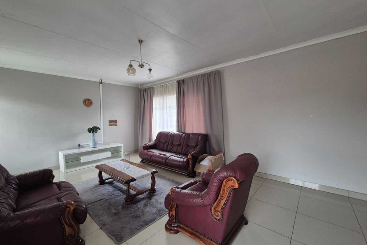 A spacious living room featuring neutral tiled flooring, large windows with curtains, and a central ceiling light fixture.