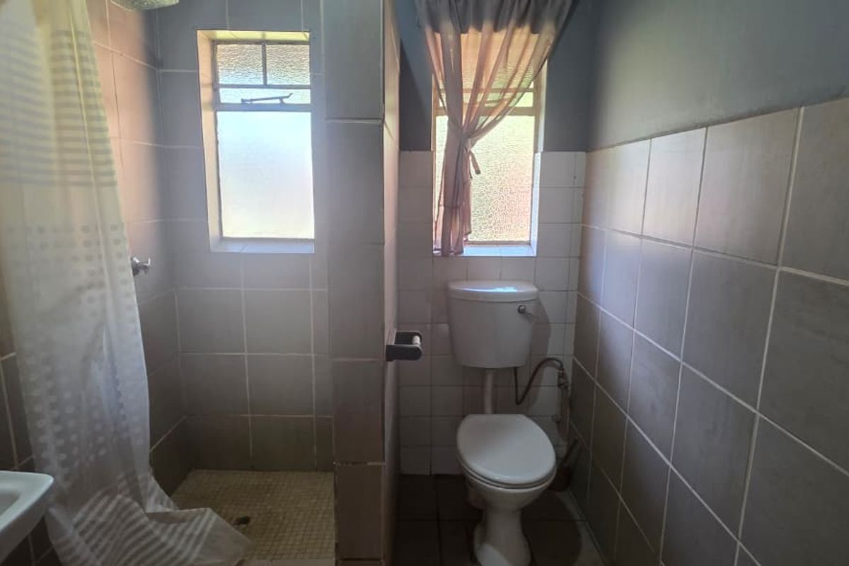A functional bathroom featuring a shower enclosure, toilet, and wall-mounted basin with tiled walls and flooring.