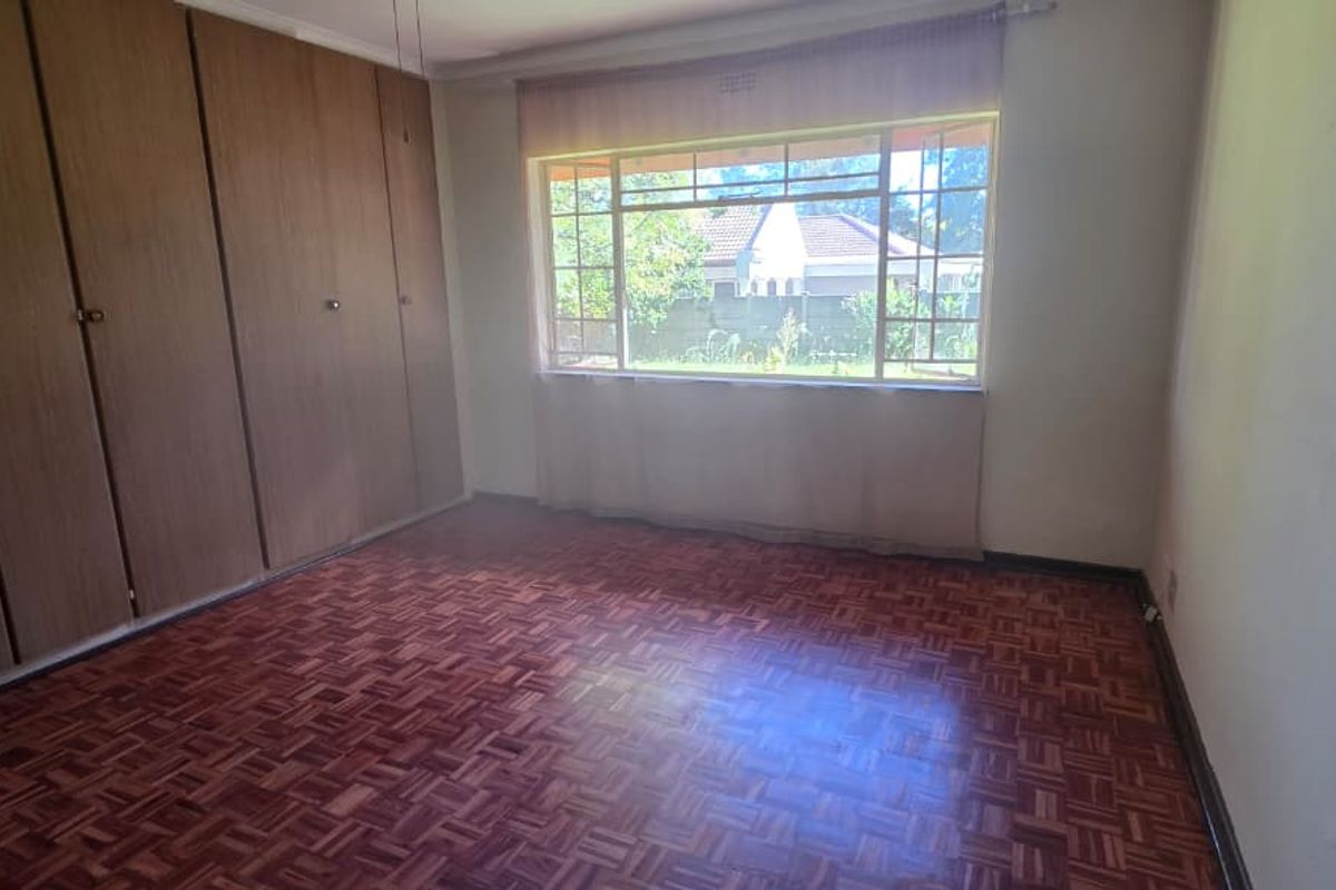 A bedroom featuring classic parquet flooring and extensive built-in wooden cupboards, offering a functional space with a view of the garden.