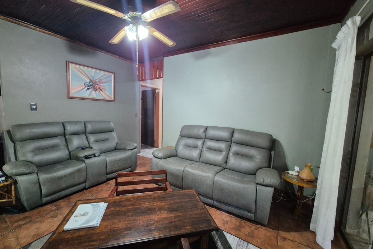 A living room featuring a dark wood paneled ceiling, ceiling fan, and terracotta-style floor tiles.