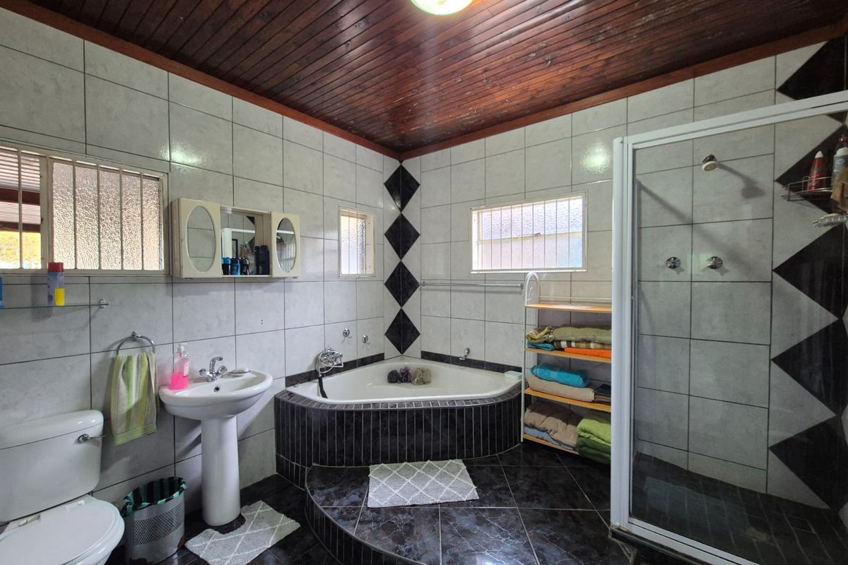 A functional bathroom featuring a corner bathtub, separate shower enclosure, pedestal basin, and toilet, finished with tiled walls and a timber-paneled ceiling.