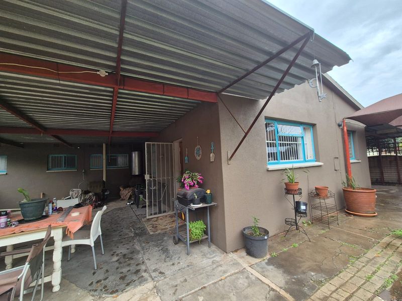 A covered outdoor patio area featuring a corrugated metal roof, steel structural supports, and paved flooring, providing a functional space for outdoor living.