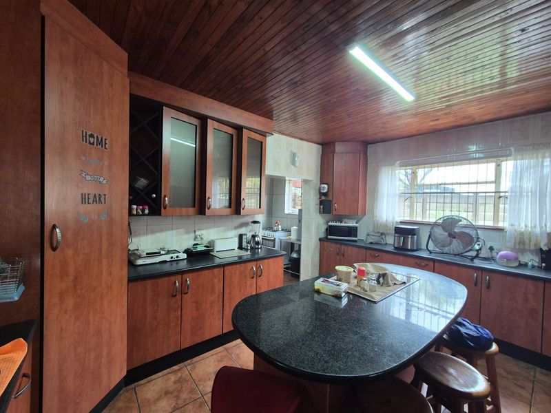 A functional kitchen featuring dark wood cabinetry, granite countertops, a central island, and a distinctive timber-paneled ceiling with tiled flooring throughout.