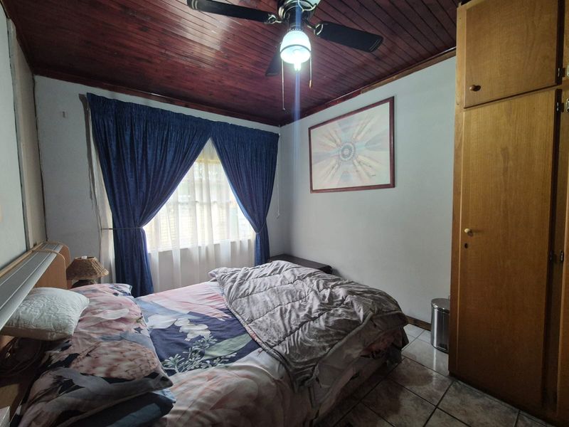 A bedroom featuring a dark timber ceiling, ceiling fan, tiled flooring, and a built-in wooden wardrobe.