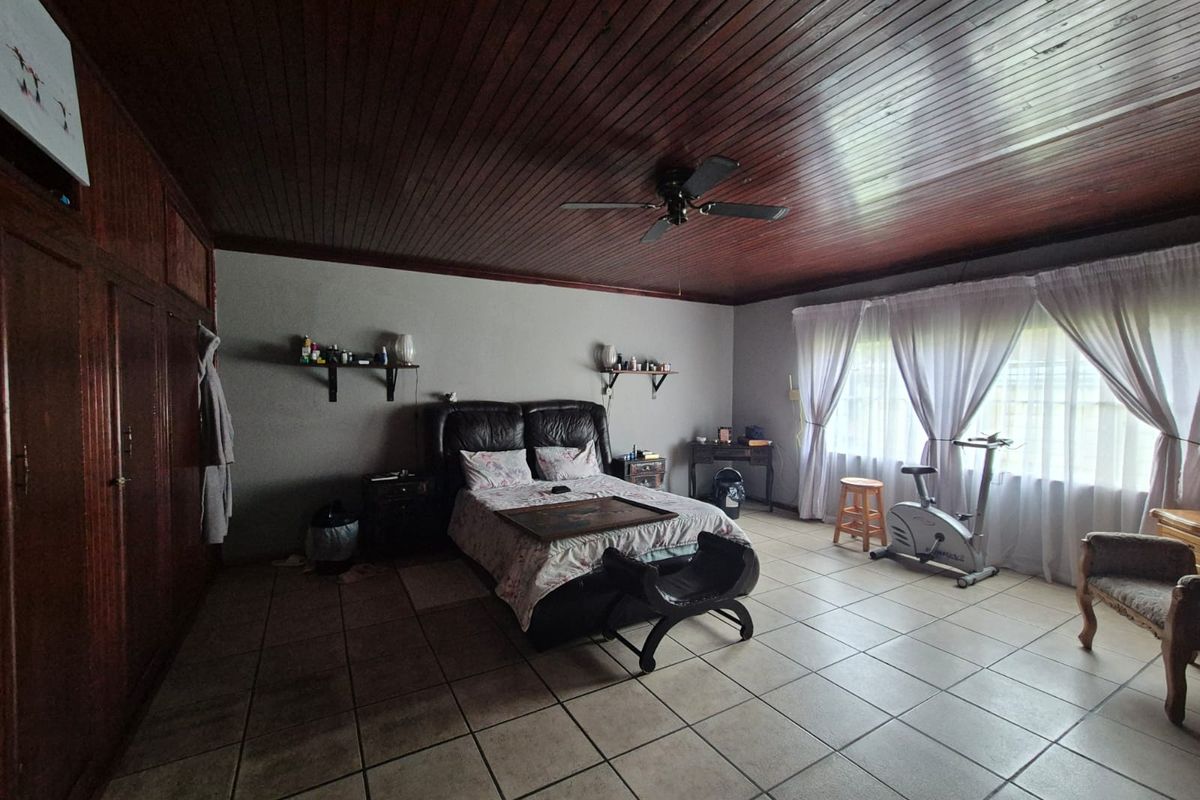 Spacious bedroom featuring tiled flooring, a timber-paneled ceiling with a ceiling fan, and extensive built-in wooden cupboards.