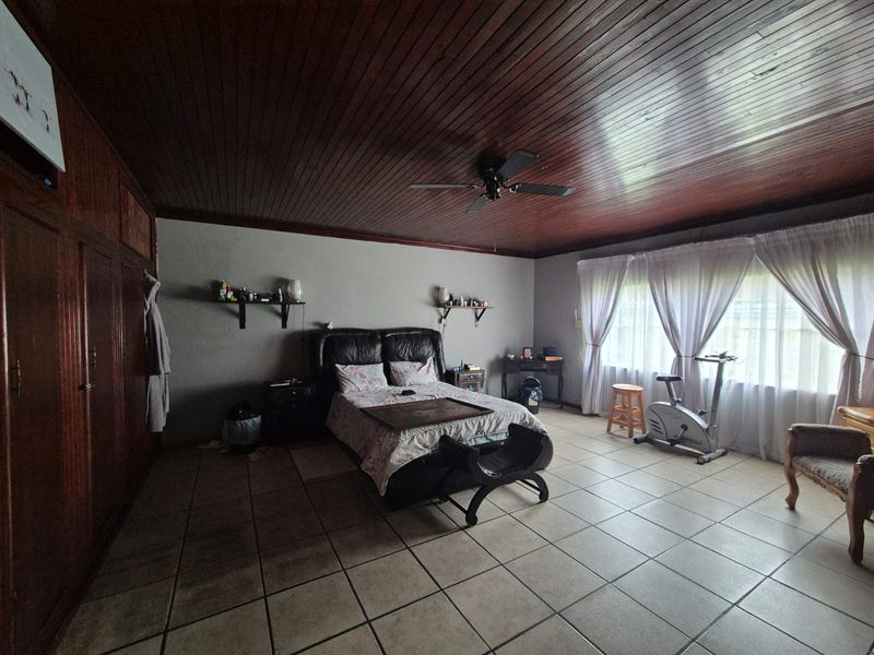 Spacious bedroom featuring tiled flooring, a timber-paneled ceiling with a ceiling fan, and extensive built-in wooden cupboards.