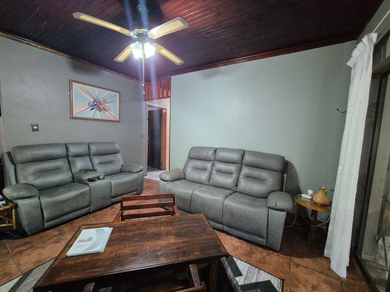 A living room featuring a dark timber ceiling, ceiling fan, and tiled flooring, providing a functional and comfortable space.