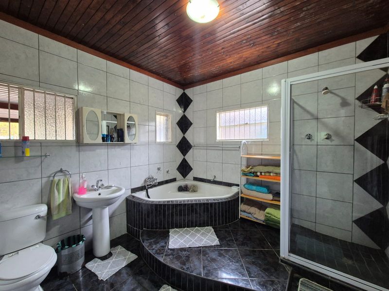 A functional bathroom featuring a corner bathtub, separate shower enclosure, pedestal basin, and tiled finishes with a timber ceiling.