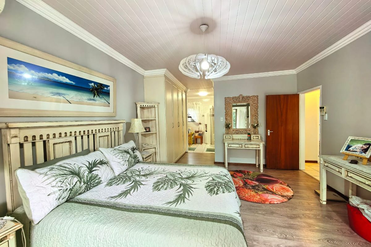 Spacious bedroom featuring built-in cupboards, wood-look laminate flooring, and a classic tongue-and-groove ceiling with crown molding.