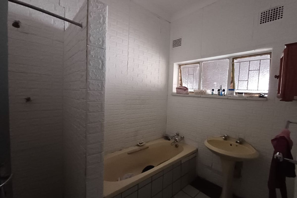 A dated bathroom featuring a built-in bathtub, pedestal basin, and shower area with textured wall finishes and natural light from a high window.