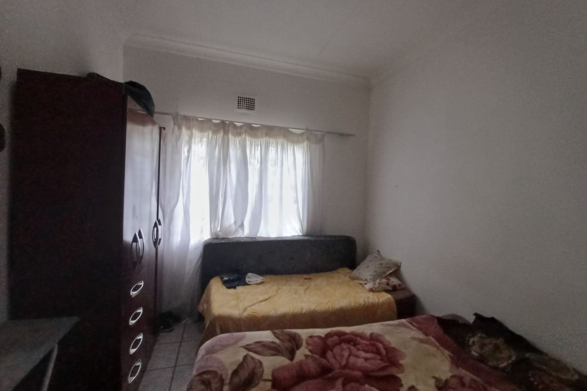 A functional bedroom featuring tiled flooring and a window with curtaining, providing a basic living space.