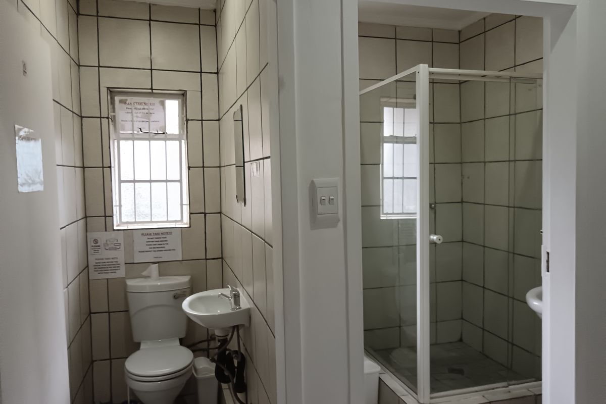 A functional bathroom featuring a toilet, wall-mounted basin, and a separate shower enclosure with tiled walls and flooring.