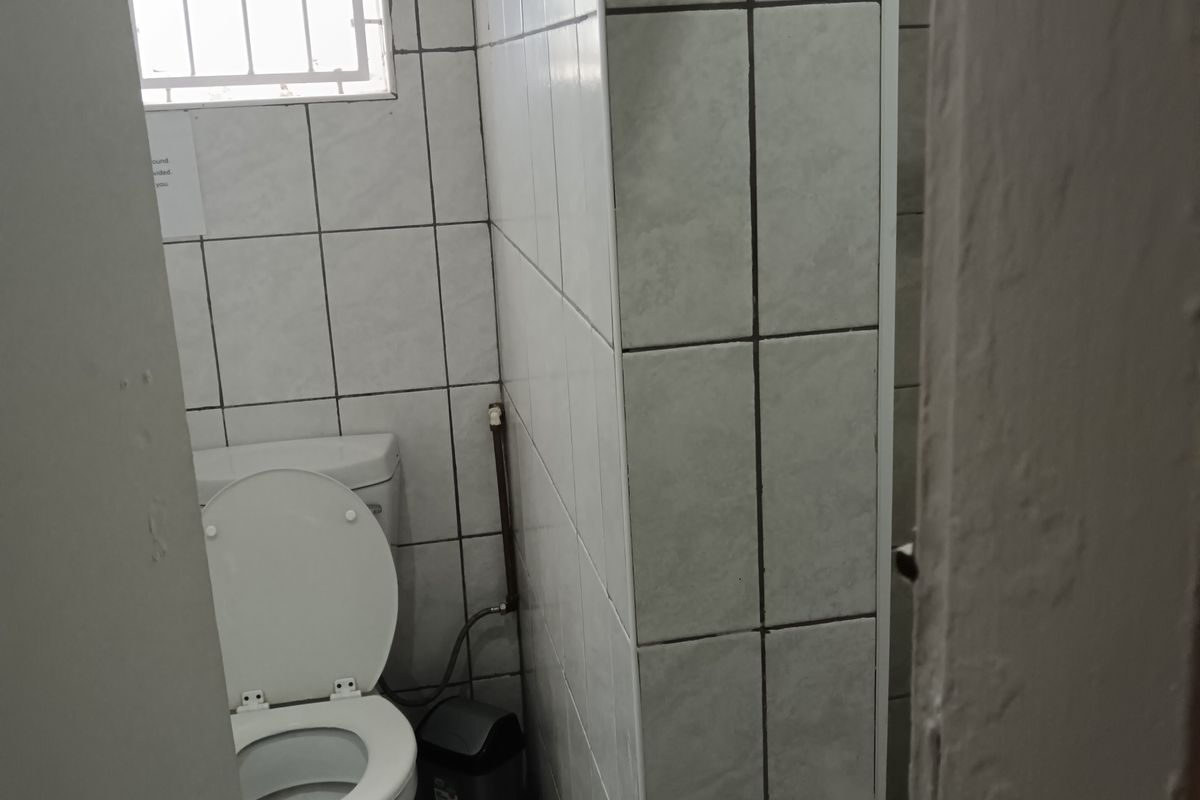 A compact bathroom featuring tiled walls and flooring, a standard toilet, and a small window with security bars.