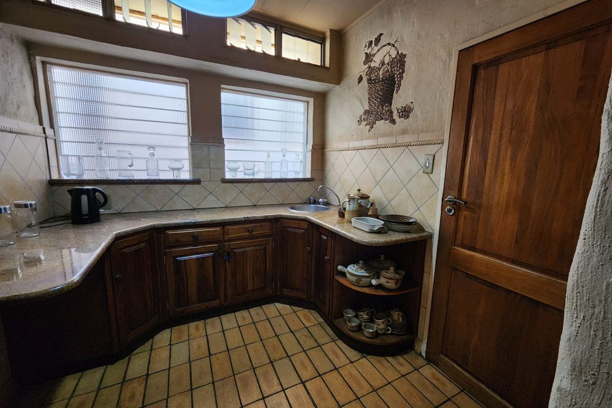 A compact kitchen featuring dark wood cabinetry, granite countertops, tiled backsplash, and a small sink, with natural light provided by high-set windows.