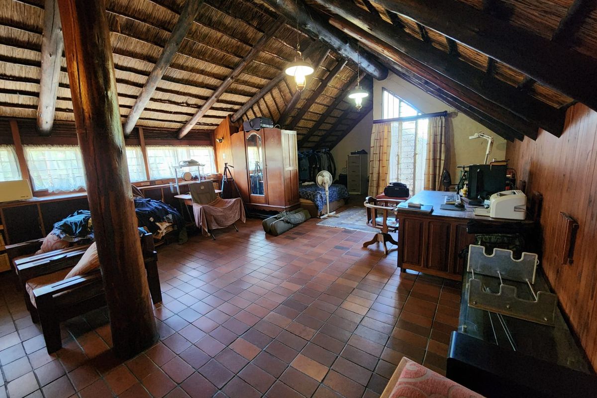 Spacious attic-style bedroom featuring a high vaulted thatched roof, exposed timber beams, and terracotta floor tiles.