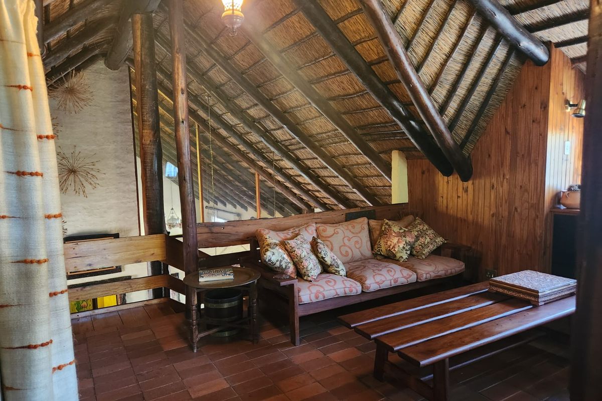 A cozy loft living area featuring a high-pitched exposed thatch roof, timber support beams, and terracotta floor tiles.