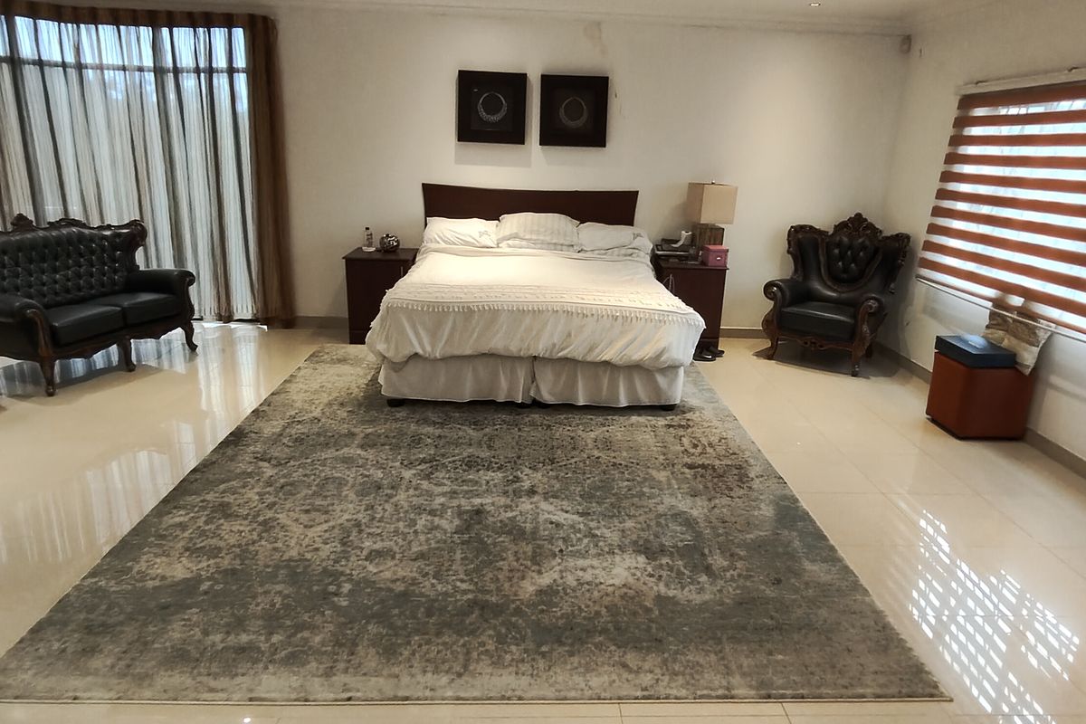 Spacious bedroom featuring large windows with blinds, floor-to-ceiling curtains, and tiled flooring. Note visible ceiling water staining requiring attention.