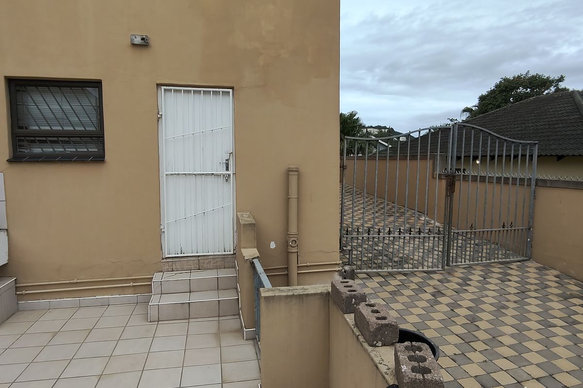 Rear exterior area featuring a tiled patio, concrete wash trough, paved driveway, and secure gated access to the property.
