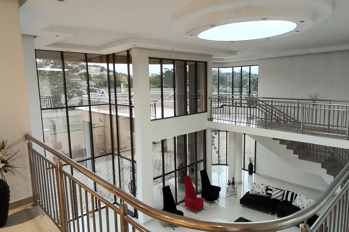 Spacious double-volume living area featuring a modern stainless steel balustrade, expansive glass windows, and elegant recessed ceiling lighting.