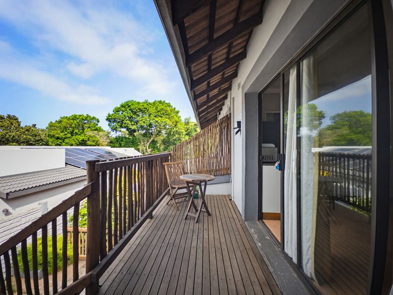 A covered wooden balcony featuring timber decking, a wooden balustrade, and sliding glass door access to the interior living space.