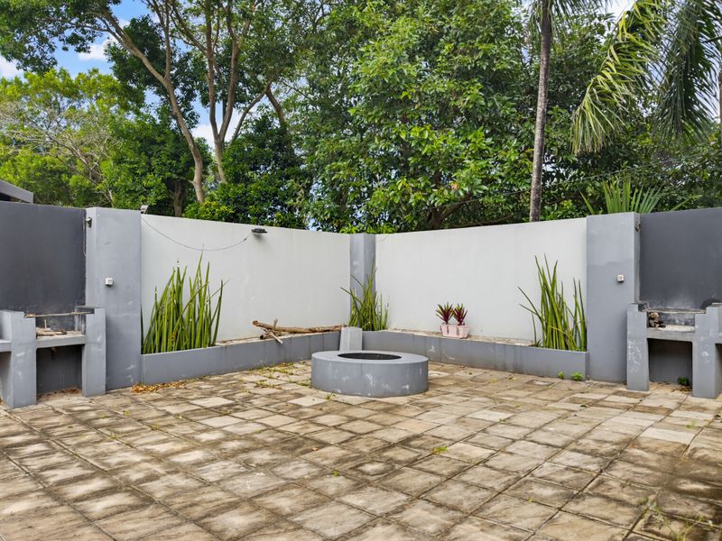 Outdoor patio area featuring a built-in fire pit and dual masonry braai stations, set against a perimeter wall with integrated garden beds.