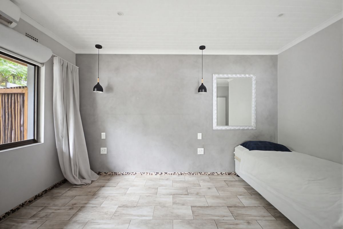 A modern bedroom featuring a feature wall with pendant lighting, tiled flooring, and a wall-mounted air conditioning unit.