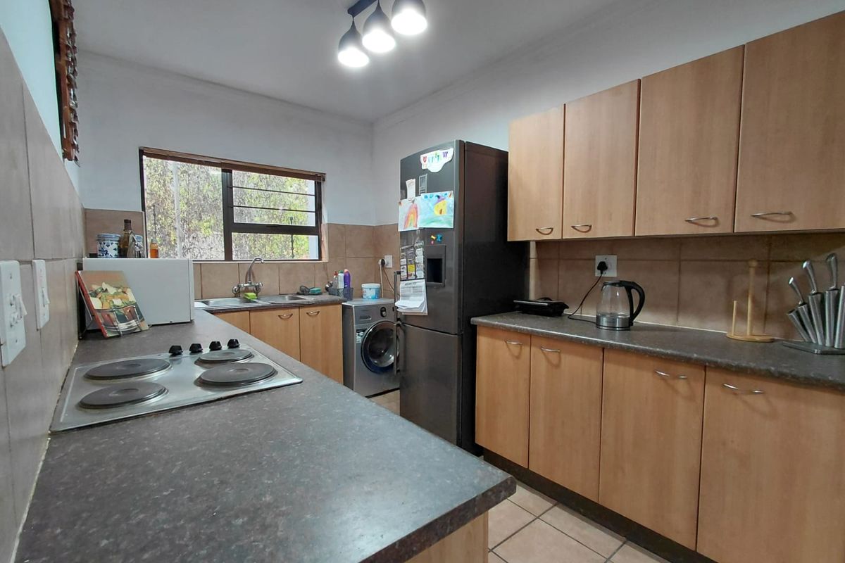 Functional kitchen featuring light wood cabinetry, dark laminate countertops, a built-in electric hob, and tiled flooring.