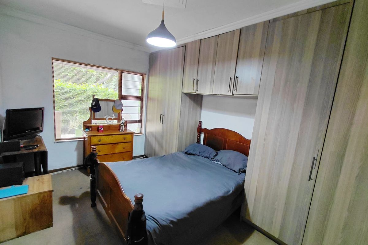 A bedroom featuring extensive built-in cabinetry with overhead storage, a large window with blinds, and a central pendant light fixture.