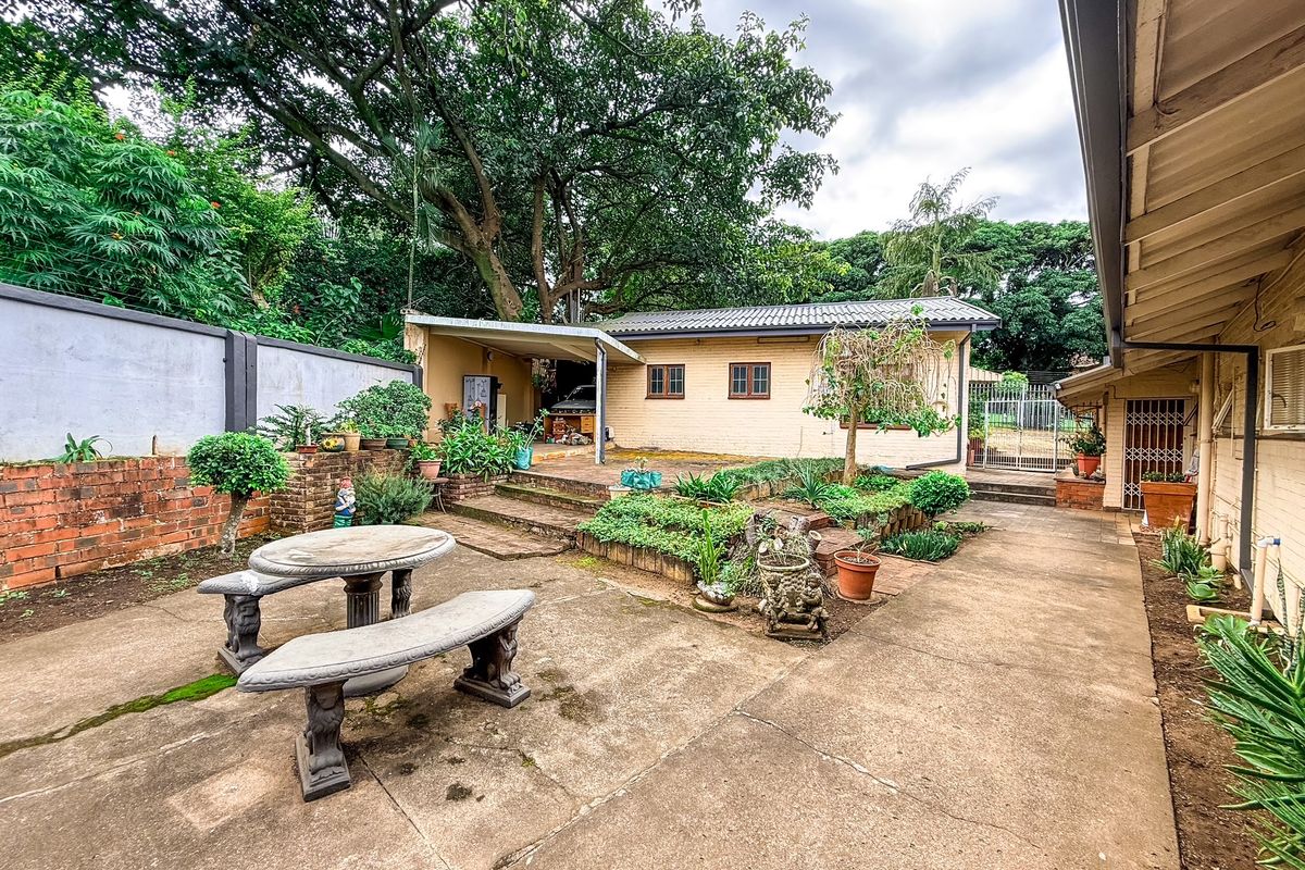 A rear courtyard featuring concrete paving, tiered garden beds, and a detached outbuilding with a covered patio area.