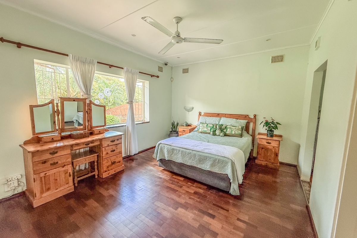 Spacious bedroom featuring polished timber flooring, a ceiling fan, and large windows allowing for natural light.